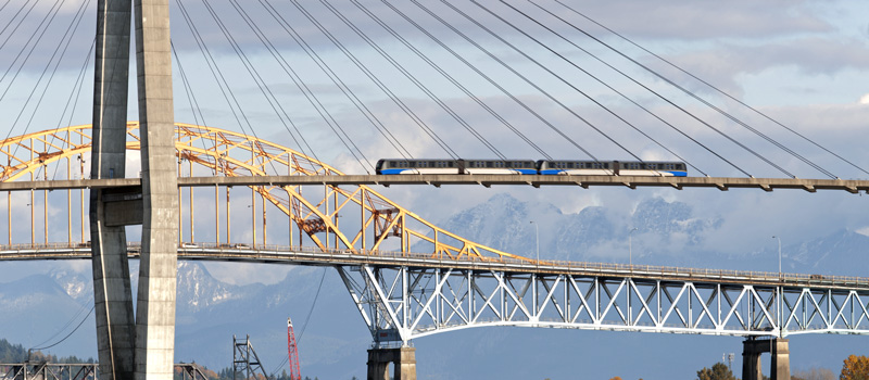 SkyTrain crossing a bridge in Vancouver with mountains in the background representing life in Canada